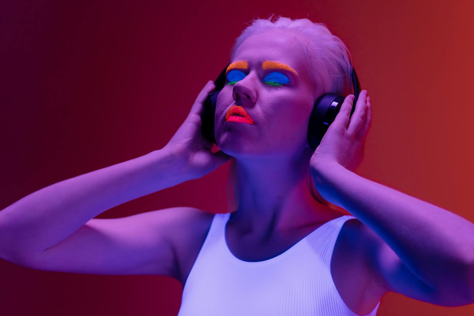 woman with bright neon make up and her eyes closed under blue light holding headset